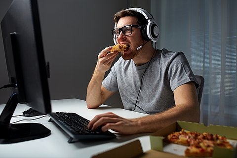 Guy eating pizza in front of a desktop screen