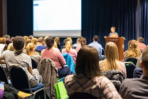 Publikum mit Sprecher vor großer Leinwand